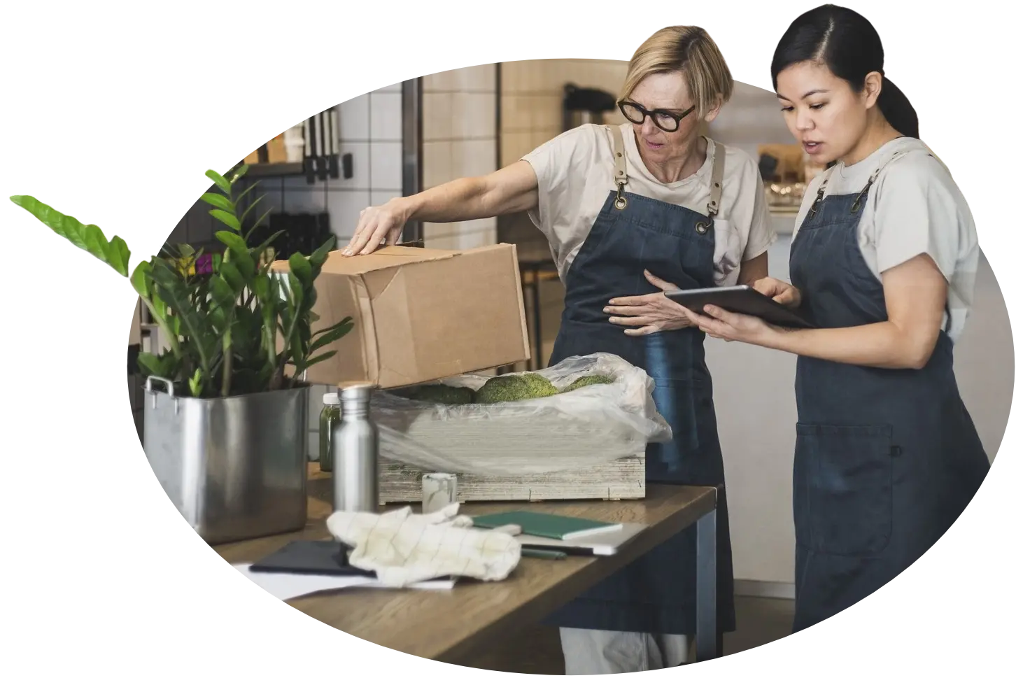 two women in aprons working at a table covered in plants