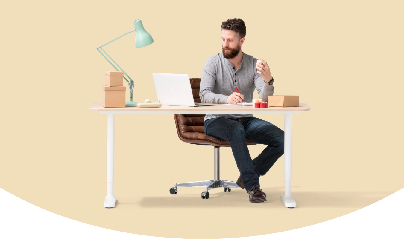man sitting at a desk looking at a laptop while writing with a pen