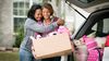 Mom hugging daughter holding box of dorm room supplies.