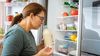 Woman smells milk in refrigerator to check for food spoilage.