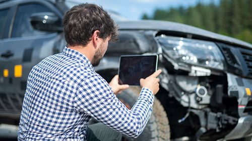 Man taking a photo of his damaged car to document for a car insurance claim.