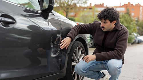 Young man examining the damage to his vehicle following a car accident.