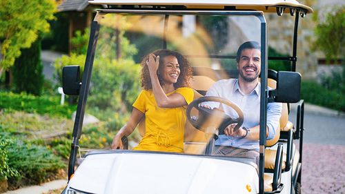 Couple driving golf cart on a path.