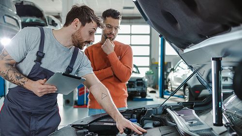 Mechanic showing a customer damages on a car at an auto body shop.