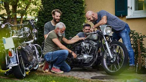 Four friends looking at their motorcycles outside a house.
