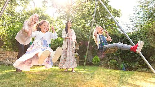 Two women pushing young girls on a backyard playground.