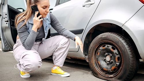 Young woman with a flat tire on the road calling for roadside assistance on her cell phone.