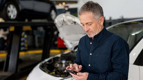 Man texts on phone at an autobody shop
