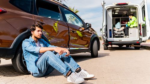 Man sitting on ground after causing an accident with ambulance in background.
